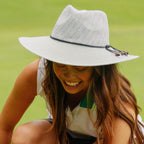 A woman smiling on a green lawn wearing a light gray woven sun hat with a black band and small decorative beads on the brim.